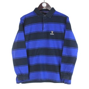 以下が含まれることがあります： 青と黒のストライプの長袖ラグビーシャツ。 シャツは襟付きネックラインと3つボタンの前立てが特徴です。 胸にはギネスのロゴが刺繍されています。