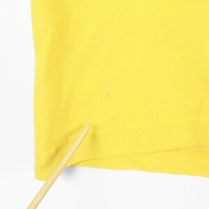 May include: A close-up of a bright yellow fabric, possibly a piece of clothing. The fabric is smooth and appears to be made of a soft material. A small, light-colored spot is visible on the fabric. A wooden stick is in the foreground.