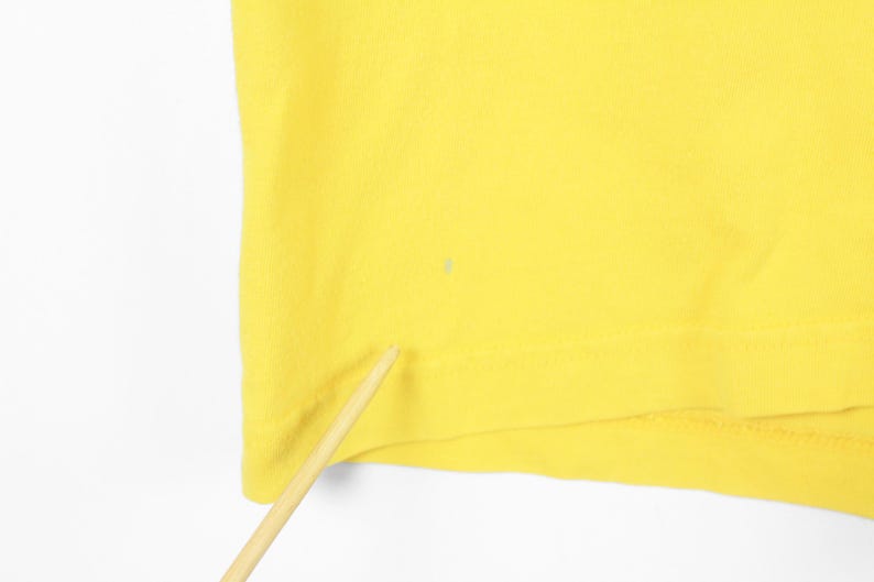 May include: A close-up of a bright yellow fabric, possibly a piece of clothing. The fabric is smooth and appears to be made of a soft material. A small, light-colored spot is visible on the fabric. A wooden stick is in the foreground.
