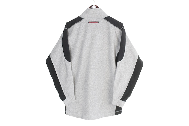 Pu&ograve; includere: Una felpa grigia con dettagli neri sulle spalle e sulle maniche. La felpa ha un collo alto e un piccolo dettaglio rosso vicino al colletto. Le maniche sono lunghe e i polsini sono a coste. La felpa &egrave; appesa a un'appendiabiti.