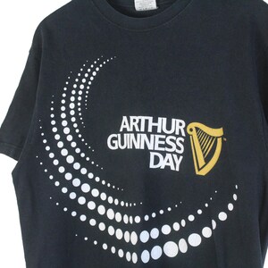 Pu&ograve; includere: T-shirt nero con la scritta "ARTHUR GUINNESS DAY" e un logo dell'arpa dorata. Un motivo a pois bianchi curvo adorna la parte anteriore. Girocollo.