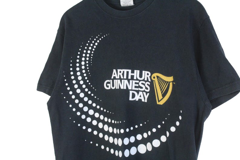 Pu&ograve; includere: T-shirt nero con la scritta "ARTHUR GUINNESS DAY" e un logo dell'arpa dorata. Un motivo a pois bianchi curvo adorna la parte anteriore. Girocollo.