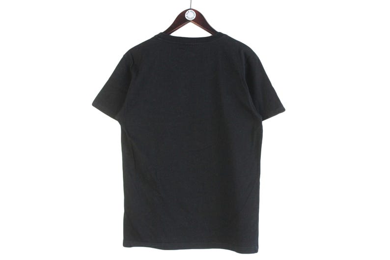 以下が含まれることがあります： 木製のハンガーに掛けられた、黒色の半袖Tシャツ。 シャツは無地で、クルーネックです。 背景は白です。