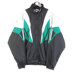 Può includere: Giacca sportiva vintage nera, bianca e verde acqua con cerniera intera. La giacca presenta un design a blocchi di colore con forme geometriche e un collo alto. La giacca è realizzata in materiale leggero.