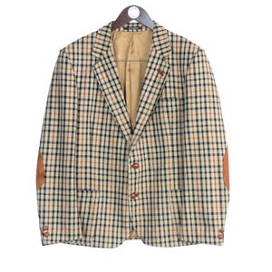 May include: A tan, black, and orange plaid blazer with brown elbow patches and buttons. The blazer has a tan lining and is hanging on a wooden hanger. A classic, vintage style.