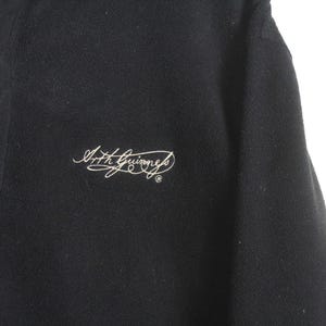 以下が含まれることがあります： 黒いポロシャツ。襟と、白い筆記体で刺繍された小さなロゴが付いています。襟には細いバーガンディのトリムが付いています。シャツは柔らかく、質感のある生地で作られています。