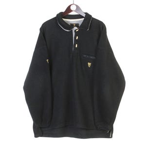 May include: Black long-sleeved pullover shirt with a collared neckline and a three-button placket. Features a small pocket on the chest and a gold-colored emblem. The shirt has a white trim on the collar and cuffs. The Guinness logo is visible.