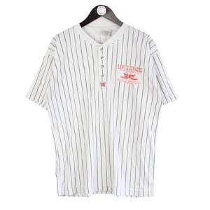 Peut inclure: Chemise à manches courtes rayée blanche et noire avec un col boutonné. La chemise porte le logo Levi Strauss en rouge sur la poitrine. La chemise est suspendue à un cintre noir.