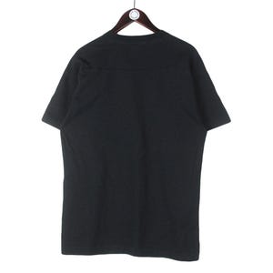 Puede incluir: Una camiseta negra lisa colgada de una percha de madera. La camiseta de manga corta est&aacute; hecha de un material suave y tiene un dise&ntilde;o sencillo. La camiseta se muestra sobre un fondo blanco.