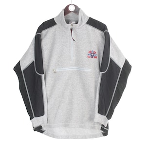 Pu&ograve; includere: Un pullover in pile grigio con pannelli neri sulle spalle e sulle maniche. Presenta una chiusura con zip a un quarto, una piccola tasca sul petto e una toppa con il logo "Police Club California" in rosso, bianco e blu.