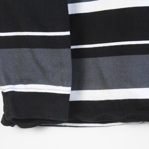 May include: Close-up of a long-sleeved shirt with horizontal stripes. The shirt features alternating stripes of black, white, and gray. The sleeve cuff is solid black. The fabric appears to be a soft knit material.