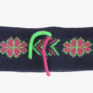 May include: A navy blue knit headband with a geometric pattern in pink and green. The headband has a green and pink drawstring. This winter accessory is designed to keep the ears warm.