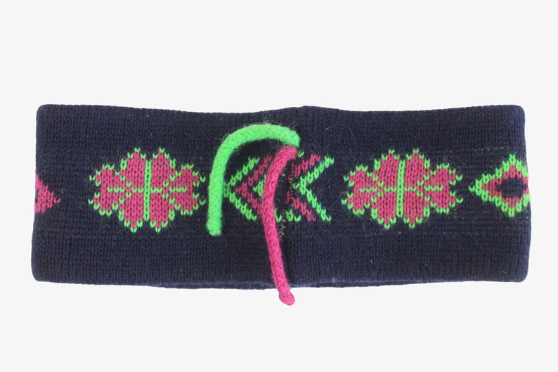 May include: A navy blue knit headband with a geometric pattern in pink and green. The headband has a green and pink drawstring. This winter accessory is designed to keep the ears warm.