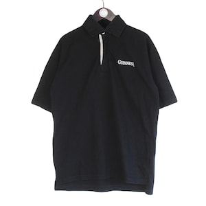 May include: Black polo shirt with short sleeves, a collared neckline, and a white placket. The word "Guinness" is embroidered in white on the chest. The shirt is hanging from a hanger.