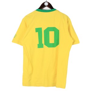 May include: Yellow short-sleeve t-shirt with a green collar and the number 10 in green on the back. The shirt is hanging on a wooden hanger.