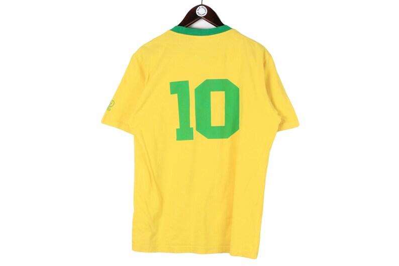 May include: Yellow short-sleeve t-shirt with a green collar and the number 10 in green on the back. The shirt is hanging on a wooden hanger.