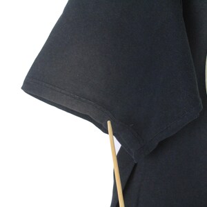 May include: Black t-shirt featuring a partial view of a Guinness logo. The logo is circular with text and a harp design. The shirt's sleeve is visible, showing the fabric's texture.