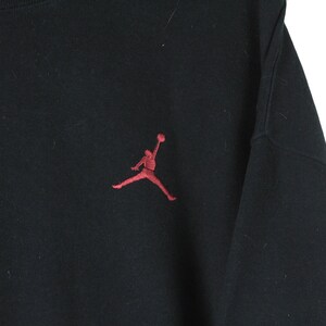 Może przedstawiać: Czarna bluza z haftowanym czerwonym logo Jordan na przodzie.