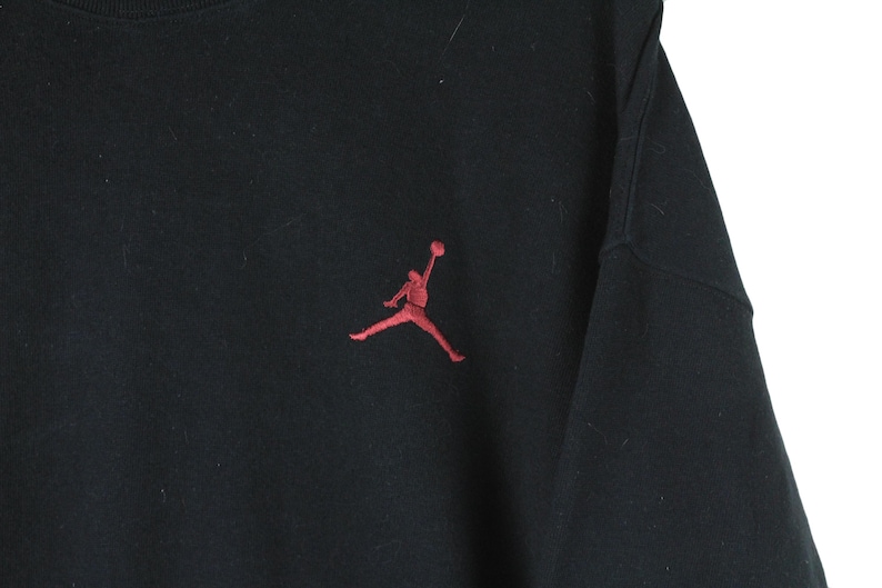 Może przedstawiać: Czarna bluza z haftowanym czerwonym logo Jordan na przodzie.