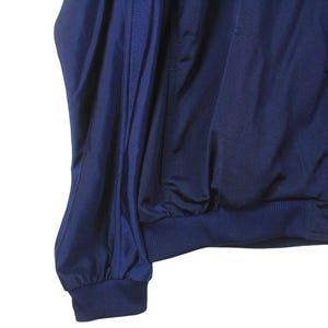 May include: A navy blue jacket with a full zipper and ribbed cuffs and hem. The jacket is made of a smooth, possibly nylon or polyester material. The sleeves are gathered at the wrist.