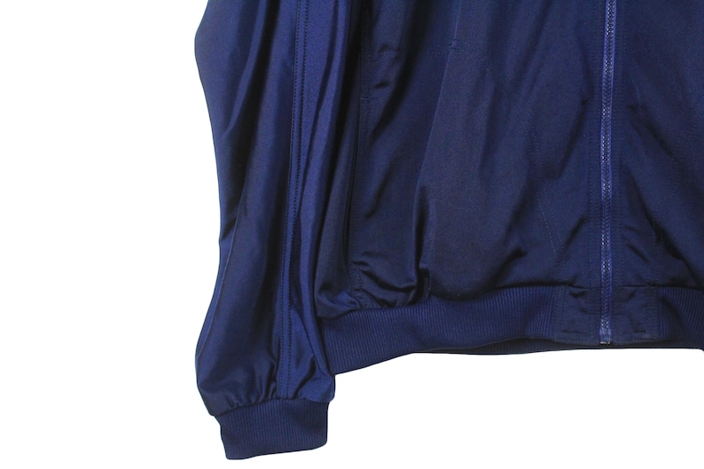 May include: A navy blue jacket with a full zipper and ribbed cuffs and hem. The jacket is made of a smooth, possibly nylon or polyester material. The sleeves are gathered at the wrist.