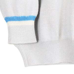Puede incluir: Primer plano de un su&eacute;ter gris claro con dobladillo y pu&ntilde;os acanalados. El pu&ntilde;o presenta un dise&ntilde;o de rayas azules y blancas. El su&eacute;ter est&aacute; hecho de un material de punto suave.
