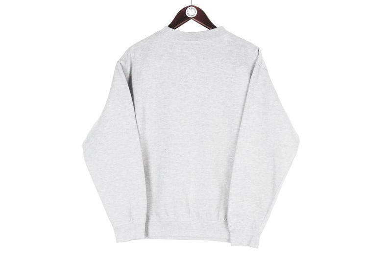 Puede incluir: Una sudadera gris claro con cuello redondo y mangas largas, colgada de una percha de madera. La sudadera tiene un dise&ntilde;o sencillo y cl&aacute;sico, adecuado para ropa informal. La tela parece ser un material suave y c&oacute;modo.