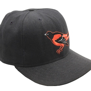 May include: A black baseball cap with a curved peak. The cap has an embroidered orange and black bird design on the front. The cap is made of a durable fabric.