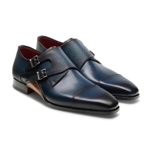 Puede incluir: Un par de zapatos de cuero azul con doble hebilla monje, con un patrón texturizado en la puntera y un tacón de cuero marrón.