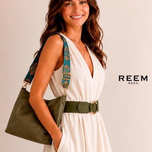 May include: An olive green shoulder bag with a wide, adjustable teal strap featuring an orange and gold floral pattern. The bag has gold-tone metal hardware and is branded with the text REEM .BAGS. on the right side of the frame.