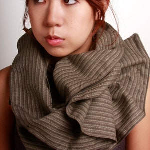 May include: A woman with long, red hair is wearing a brown and white striped scarf. The scarf is folded and draped around her neck, with the ends hanging down her chest.