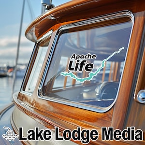 May include: A vinyl decal applied to the window of a wooden boat cabin. The decal features the text Apache Life in black and white lettering, accompanied by a light blue graphic outline of a lake shape, with Lake Lodge Media text below.