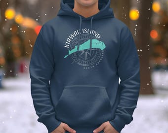 May include: A navy blue hooded sweatshirt featuring a light teal graphic of Kiawah Island, South Carolina, overlaid on a compass rose design. The text Kiawah Island and South Carolina is printed in white around the circular compass graphic.