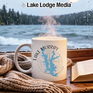 May include: A white ceramic mug featuring a light blue map silhouette of Lake Murray, Oklahoma, overlaid on a grey compass rose design. The text Lake Murray is printed in black above the map, with steam rising from the mug's opening.