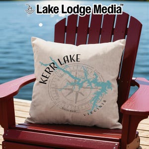 May include: A square off-white throw pillow featuring a light blue map of Kerr Lake, Virginia, overlaid with a compass rose graphic. The text "KERR LAKE" is printed in black above the map, with "VIRGINIA" printed in black along the lower right side.