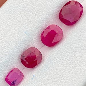 May include: Four pink oval-shaped gemstones on a white surface.