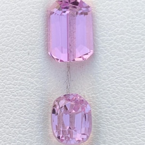 Puede incluir: Dos gemas facetadas de color rosa claro. La gema superior es rectangular con esquinas cortadas, mientras que la gema inferior es ovalada. Ambas piedras tienen un alto grado de claridad y están sobre un fondo blanco.