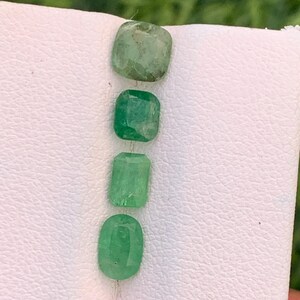 以下が含まれることがあります： 垂直に並べられた4つのルースエメラルド。クッションカット、2つの長方形のエメラルドカット、オーバルカットなど、形状は様々です。それぞれの宝石は、天然のインクルージョンを含む独特の緑色の色合いを呈しています。