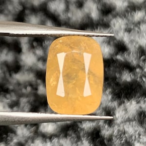 May include: A yellow oval-shaped gemstone with a faceted cut. The gemstone has a translucent appearance with a slight shimmer.
