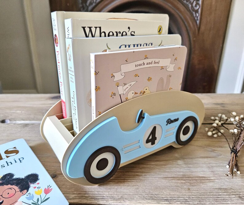 May include: A light blue and beige wooden book organizer shaped like a vintage race car. The car has black wheels, the number 4, and the name "Rome" on the side. Several children's books are inside the organizer.