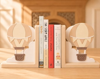 Sujetalibros con forma de globo aerostático, decoración infantil escandinava en tonos pastel, soportes personalizados para libros en estanterías infantiles.