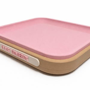 Puede incluir: Una bandeja rectangular rosa con esquinas redondeadas descansa sobre una base beige. Una etiqueta blanca en el lateral dice "YA'S TONIEBOX" en letras rosas. La bandeja est&aacute; dise&ntilde;ada para guardar objetos peque&ntilde;os.