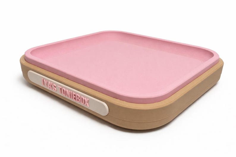 Puede incluir: Una bandeja rectangular rosa con esquinas redondeadas descansa sobre una base beige. Una etiqueta blanca en el lateral dice "YA'S TONIEBOX" en letras rosas. La bandeja est&aacute; dise&ntilde;ada para guardar objetos peque&ntilde;os.