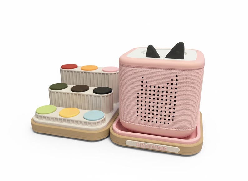 Puede incluir: Un juego de juguetes para ni&ntilde;os rosa y beige. El juego incluye un altavoz rosa con orejas de gato negras y un dise&ntilde;o de cara de gato perforada. Tambi&eacute;n hay una estructura de varios niveles con cojines circulares de colores. La base del altavoz tiene el texto "TONS TOYBOX".