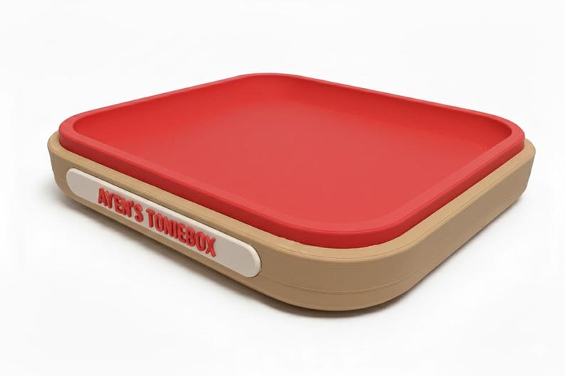 Puede incluir: Una caja de almacenamiento rectangular con interior rojo y exterior beige. La caja tiene esquinas redondeadas y una etiqueta blanca con el texto "AYEN'S TONIEBOX" en rojo. La caja est&aacute; dise&ntilde;ada para guardar objetos.