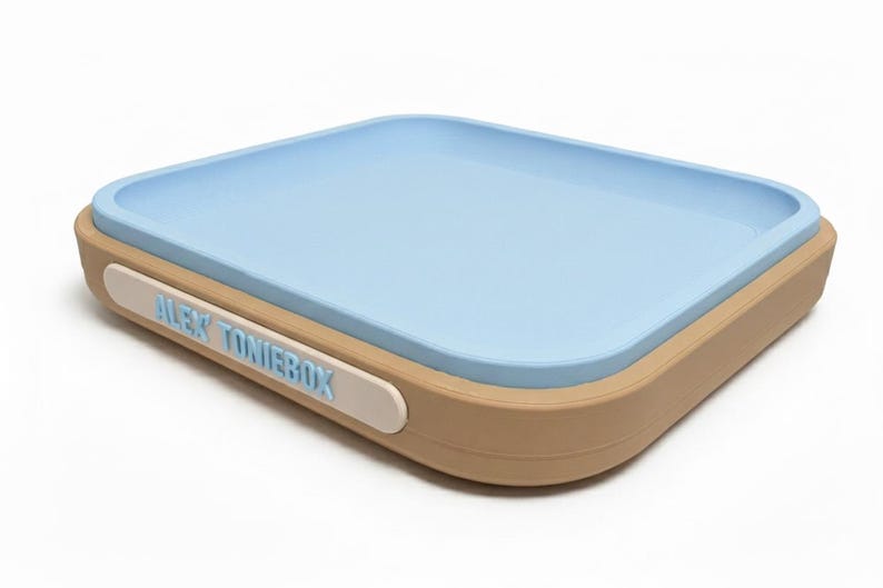 Puede incluir: Un contenedor rectangular con interior azul claro y exterior beige. El contenedor tiene bordes redondeados y una etiqueta blanca con el texto "ALEX TONIEBOX" en azul claro.