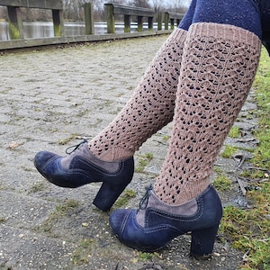 May include: A pair of knee-high, light brown knit socks featuring an intricate, openwork lace pattern with ribbed cuffs at the top. The socks are paired with dark blue, lace-up heeled shoes that have a suede-like texture on the side panels.