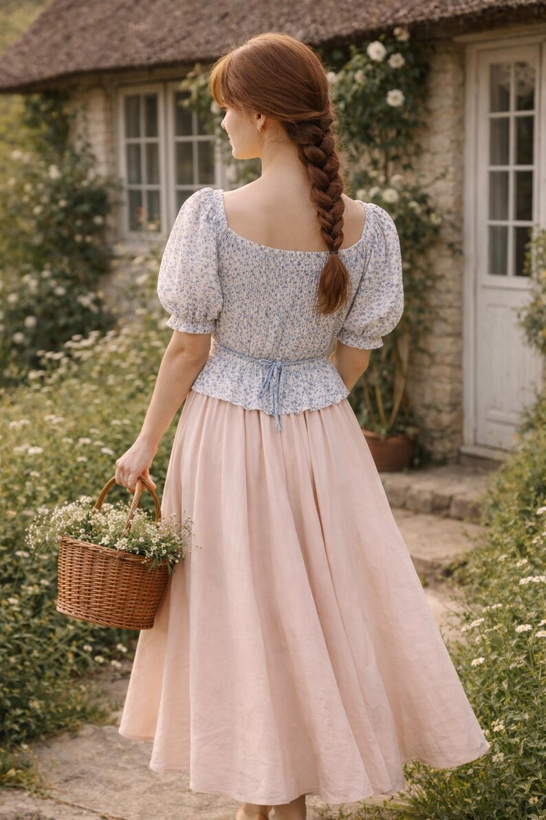 May include: A woman in a floral print top and a long pink skirt carries a woven basket filled with white flowers. The outfit has a light blue tie at the waist. The woman has long red hair in a braid.