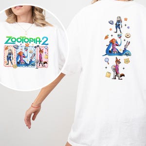 May include: White t-shirt featuring the text "Zootopia 2" in green and blue. The front graphic includes cartoon characters. The back of the shirt has additional character graphics. The shirt is made of a soft material.