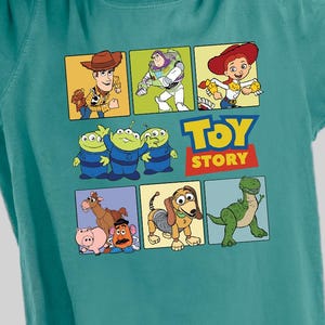 Pu&ograve; includere: Una maglietta blu turchese con una stampa grafica di personaggi del film Toy Story. La grafica include Woody, Buzz Lightyear, Rex e altri personaggi. Il testo "Toy Story" &egrave; stampato sotto la grafica.